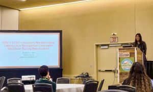 A woman stands behind a podium smiling as she answers questions related to her conference presentation